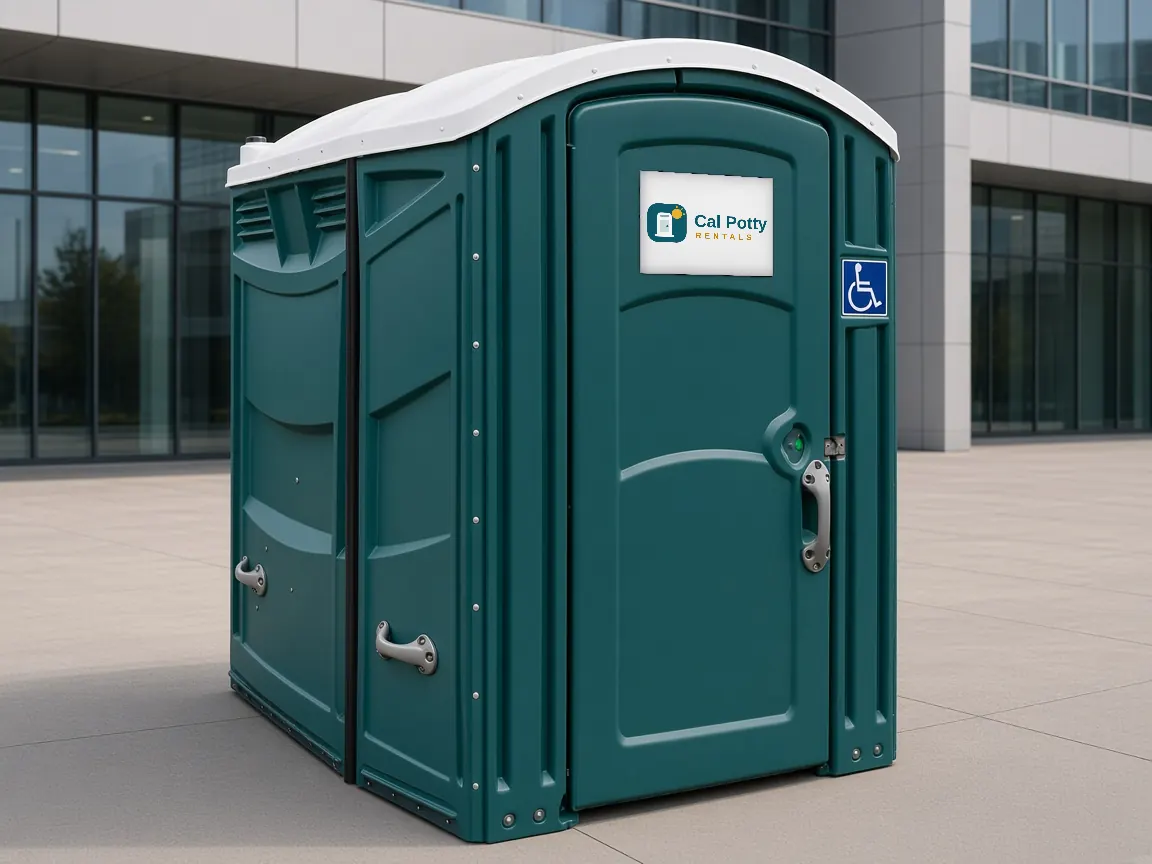 A teal ADA-accessible portable restroom with a wheelchair sign on a concrete plaza in front of a glass office building